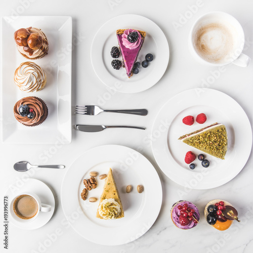 top view of arrangement of pieces of various cakes on plates, cups of coffee and cupcakes isolated on white