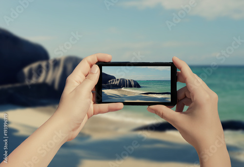 Female hand taking picture of La Digue island on mobile phone. Picture of Seychelles island on smart phone