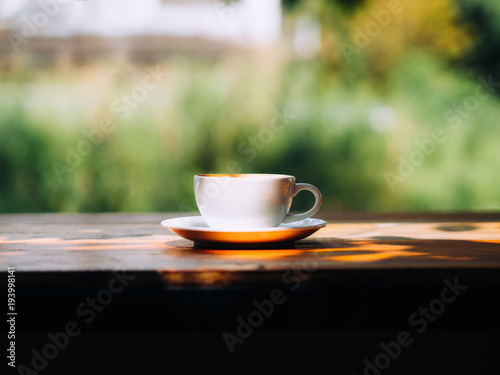 White hot cup of Latte coffee on wooden table in shadow shade.