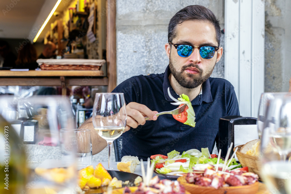 Young man eating vegetable salad and pulpo a la Gallega with potatoes. Galician octopus dishes. Famous dishes from Galicia, Spain. Young man eating vegetable salad and pulpo a la Gallega with potatoes. Galician octopus dishes. Famous dishes from Galicia, Spain.