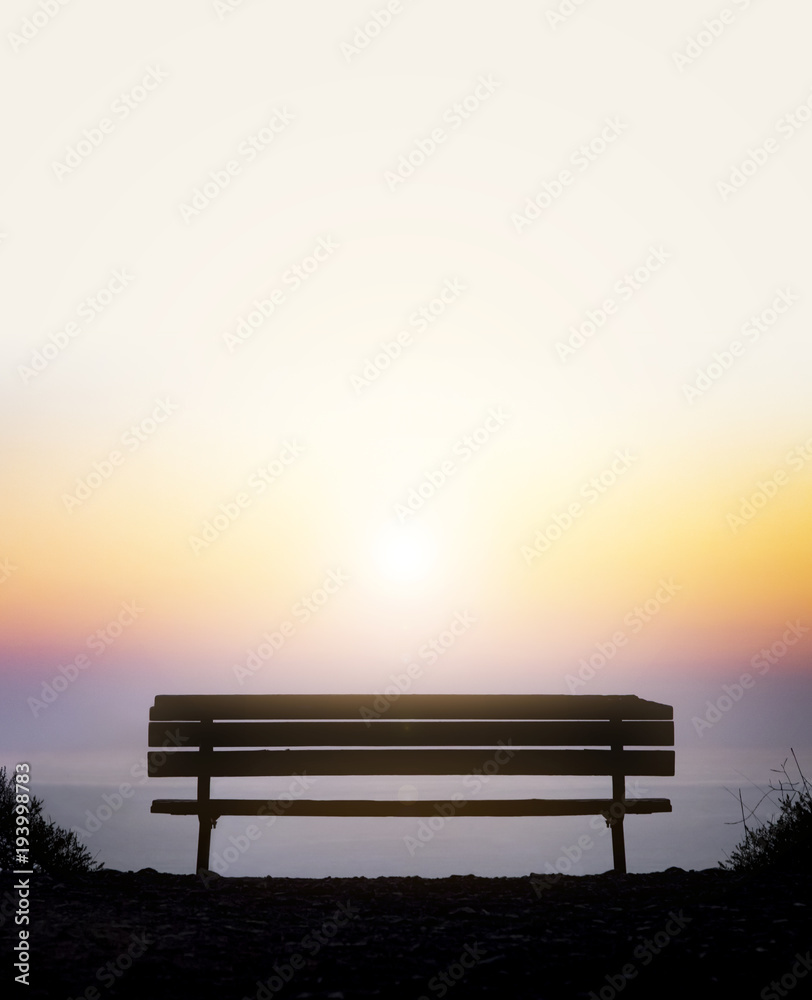 Old wooden bench overlooking a colorful sunset above the foggy ocean horizon Old wooden bench overlooking a colorful sunset above the foggy ocean horizon