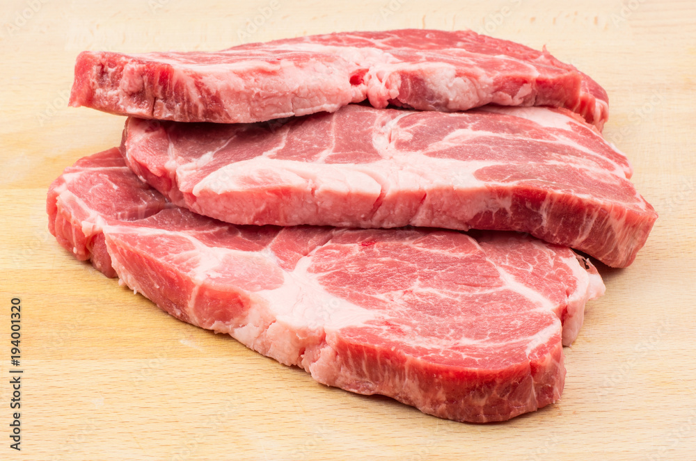 Raw pork neck three meat cuts isolated on wood background fresh slices without bone .