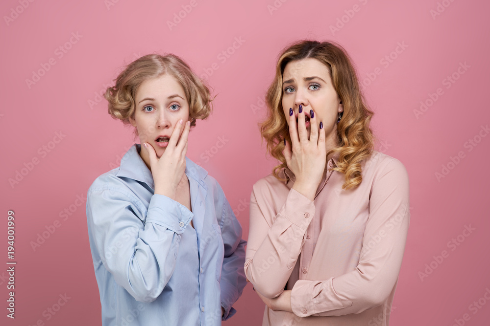 young attractive girls shocked and very surprised. Their eyes are wide open and their mouths open. Fear in their eyes is caused by a terrible incident. Studio portrait on pink background