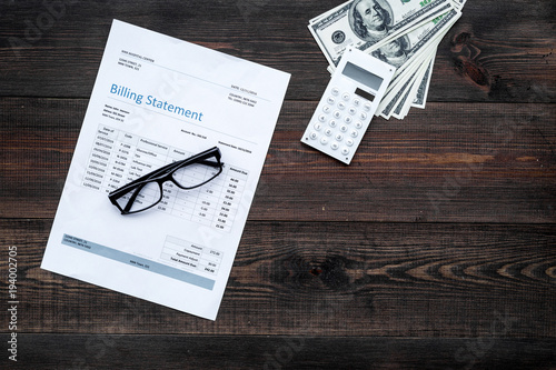 Paying bills. Billing statement near calculator, money, glasses on dark wooden background top view copy space