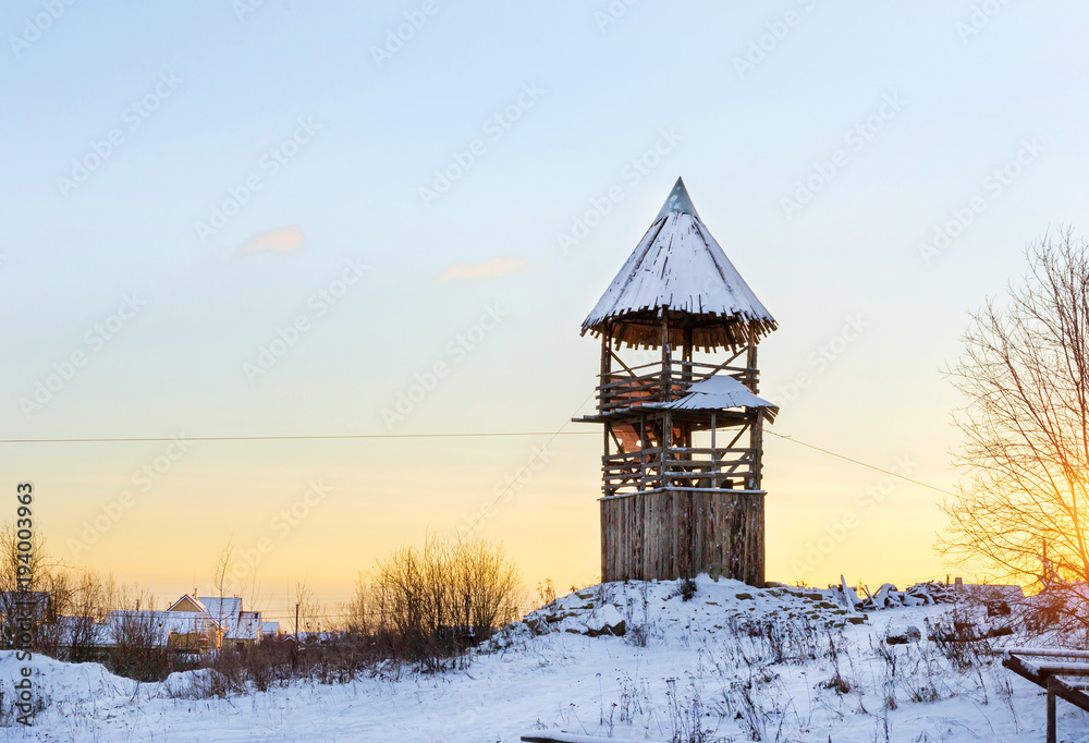 Wooden lookout tower stands on a snowy mountain. Winter landscape at sunset. Decorations of old Russian fortifications in Funny Nicholas Fortress Wooden lookout tower stands on a snowy mountain. Winter landscape at sunset. Decorations of old Russian fortifications in Funny Nicholas Fortress