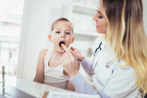 Female doctor examining child with tongue depressor at surgery  medicine  healthcare  pediatry and people concept