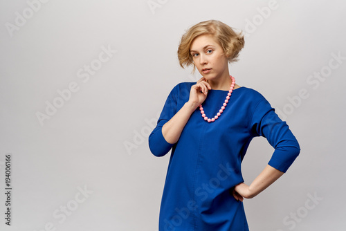a large highly detailed Studio portrait of a beautiful young blonde woman in a stylish blue dress and beads looks expressively at the camera.