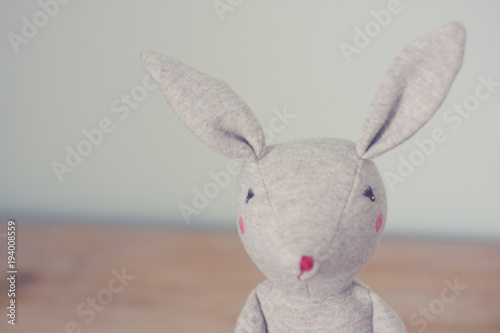 Cute toy bunny close up with natural background. Single object  light beige. Shallow depth of field. Easter bunny. Minimalistic. Matte vintage filter.