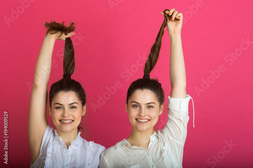 two beautiful joyful young girls sister sisters on a pink background gesture with emotional expressions of faces