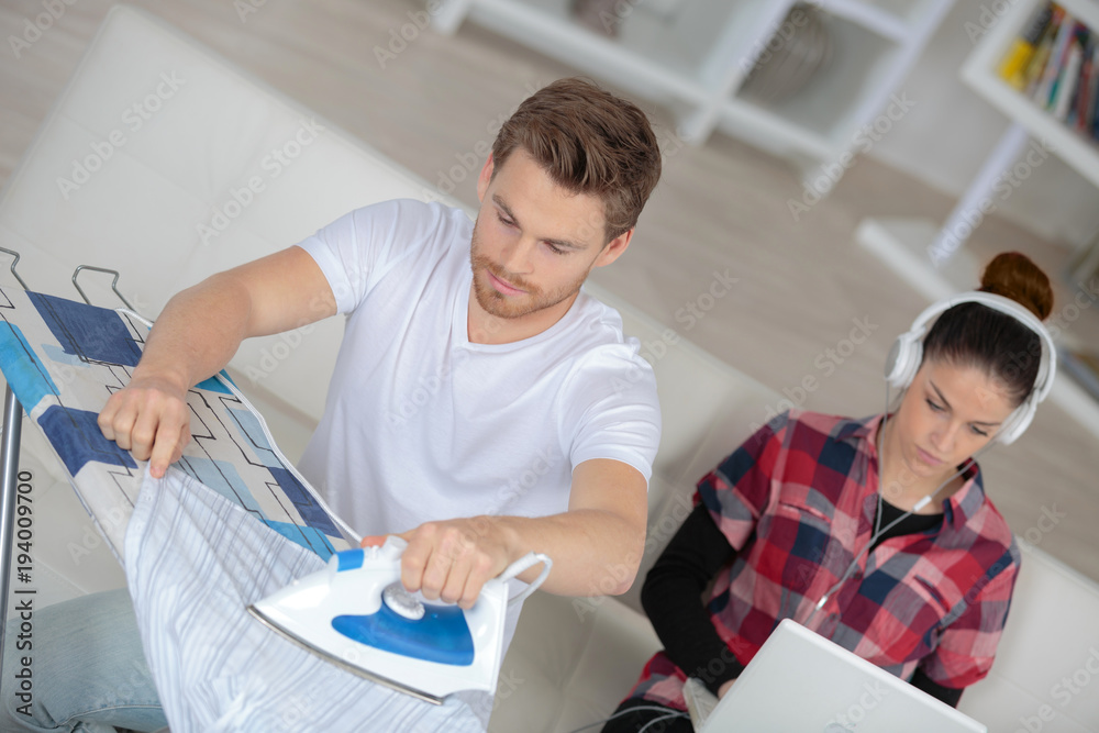 boyfriend is ironing while girlfriend is relaxing on the sofa