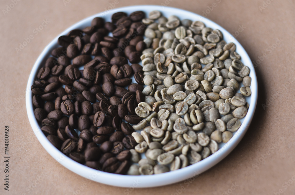 Fototapeta premium Green and roasted coffee beans divided in half on white round plate on craft paper