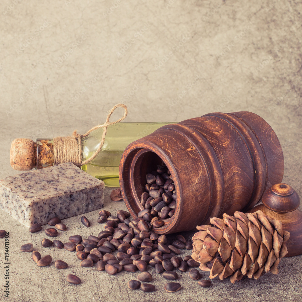 Φωτογραφία Cedar cone, wooden barrel with nuts, a piece of natural handmade soap and a small glass bottle with oil on a gray background