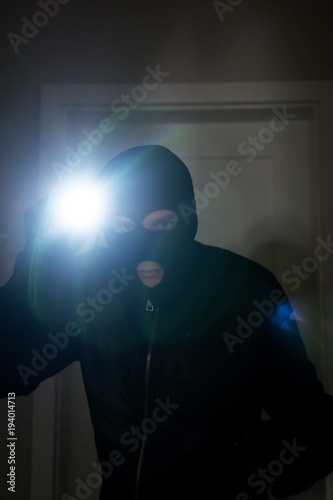 Thief wearing mask with a flashlight in the house.