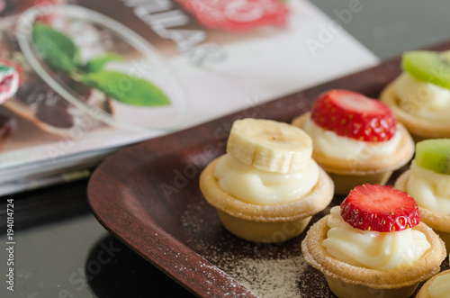 cream filled tartlets. There are strawberries, kiwi and bananas on the surface.