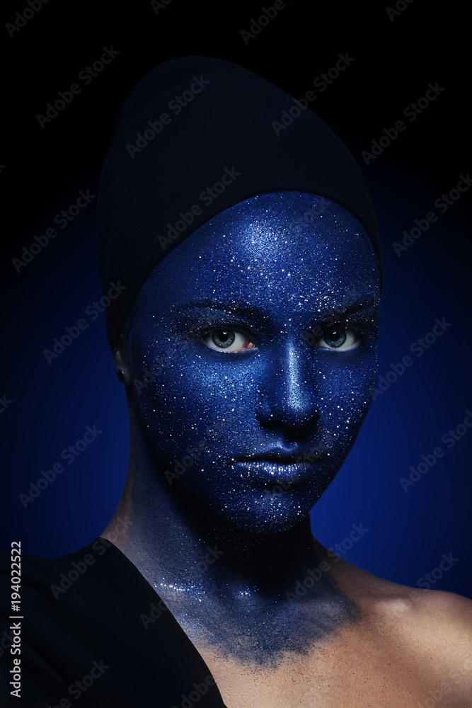 portrait of young beautiful girl. face painted with blue paint and glitter.