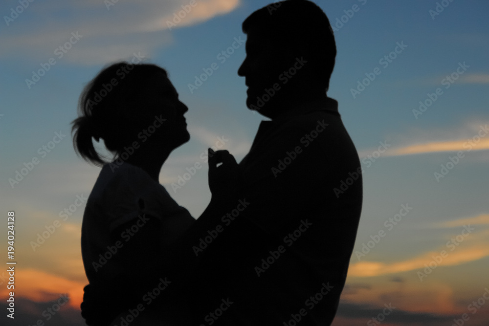 Young couple silhouette against sunset sky. Romantic evening.