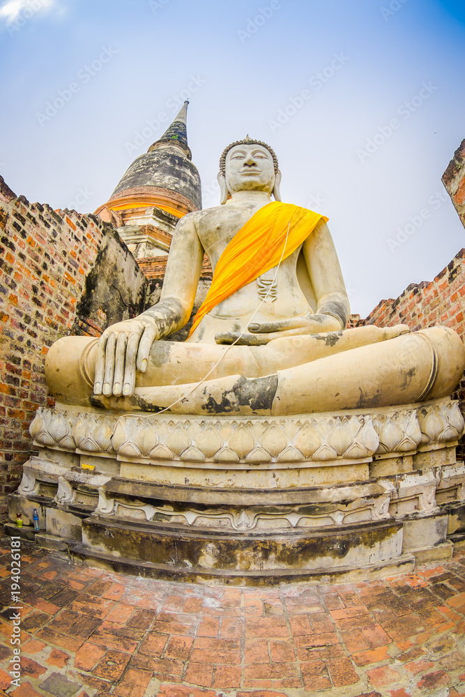 Fototapeta premium Below view of white budha with a yellow fabric around his body at Sukhothai historical park the old town of Thailand Ancient Buddha Statue at Wat Mahathat in Sukhothai Historical Park,Thailand