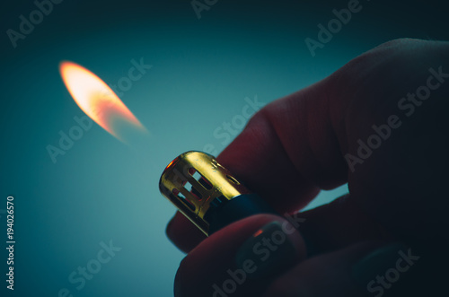 Lighter finger burning fire on green blue background