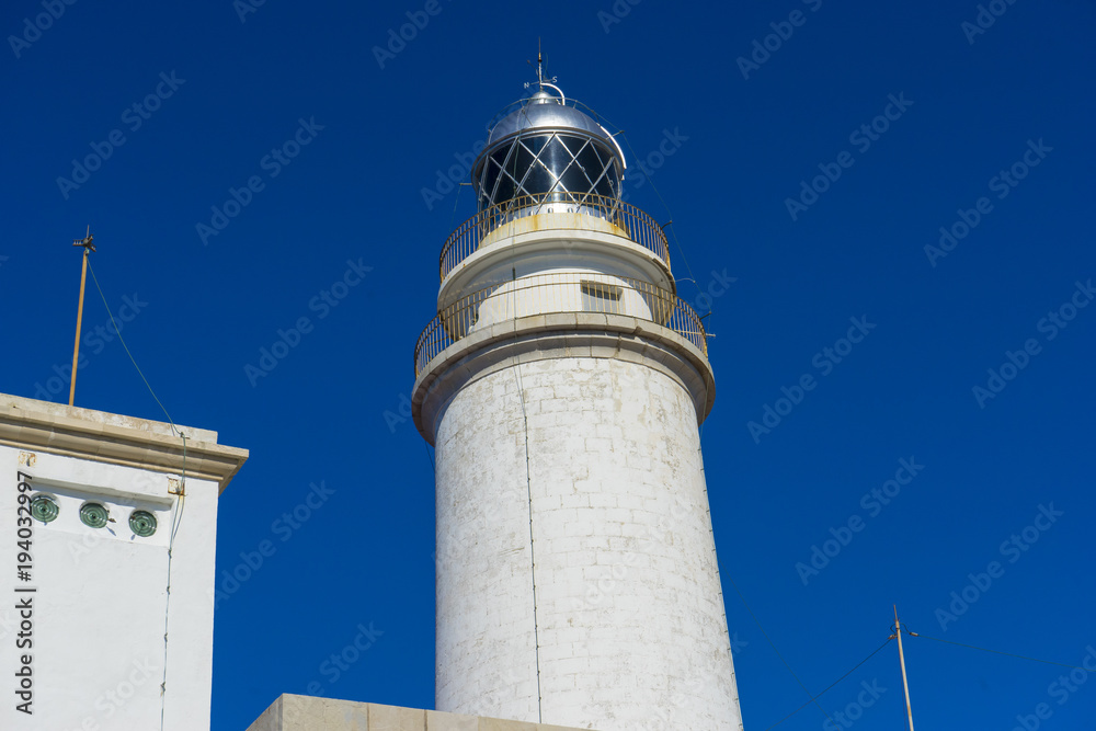 Mallorca, lighthouse next to the Mediterranean Sea, blue sky without clouds with calm waters. serves to warn ships of the presence of rocks Mallorca, lighthouse next to the Mediterranean Sea, blue sky without clouds with calm waters. serves to warn ships of the presence of rocks