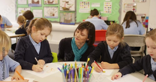 4K Primary school children drawing in the classroom with teacher helping. Slow motion