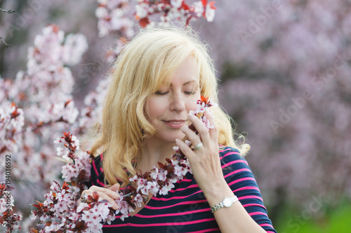 Portrait of Caucasian woman with long blond hair smelling a blossoming bunch of plum tree, eyes down