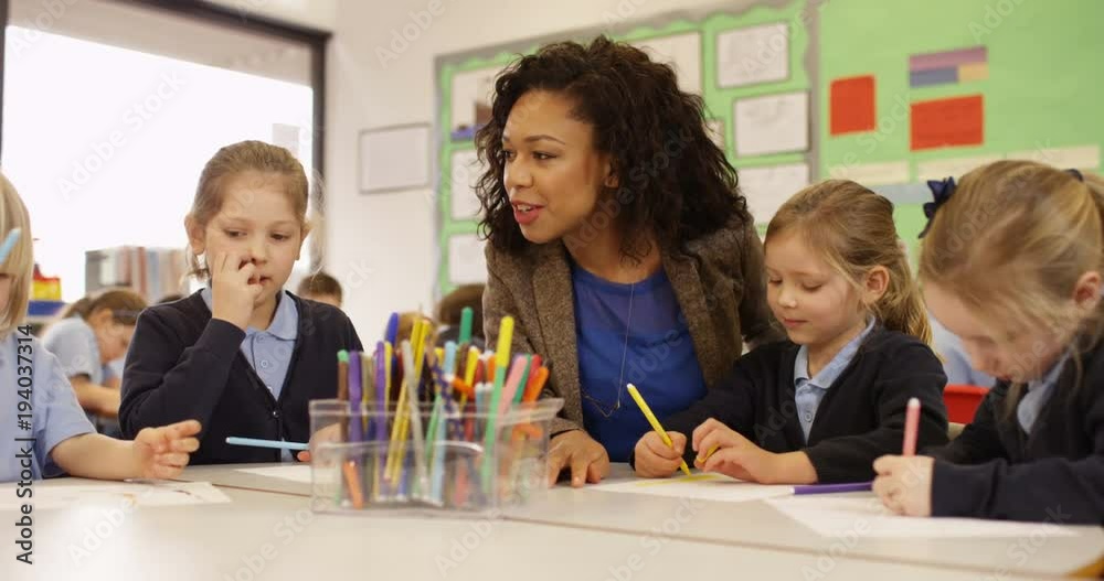 4K Primary school children drawing in the classroom with teacher helping. Slow motion