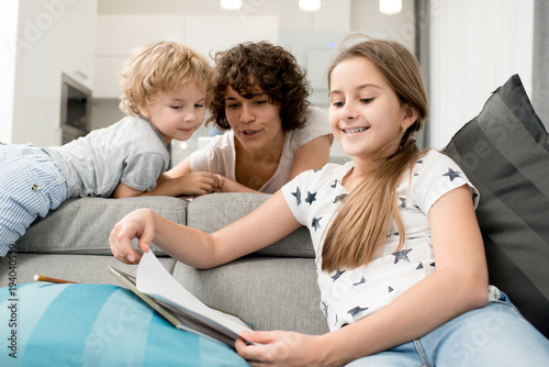 Portrait of young mother spending time at home with two children, helping teenage girl with homework