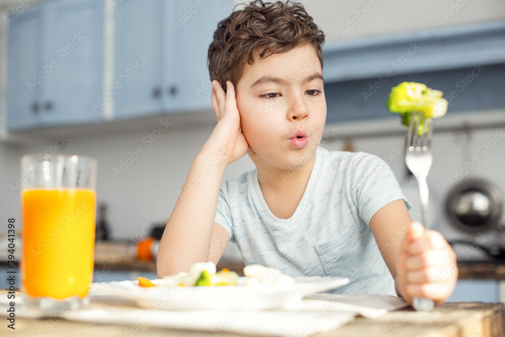 I want cookies. Handsome upset dark-haired little boy having healthy breakfast and drinking some juice and looking at the green vegetable on his fork I want cookies. Handsome upset dark-haired little boy having healthy breakfast and drinking some juice and looking at the green vegetable on his fork