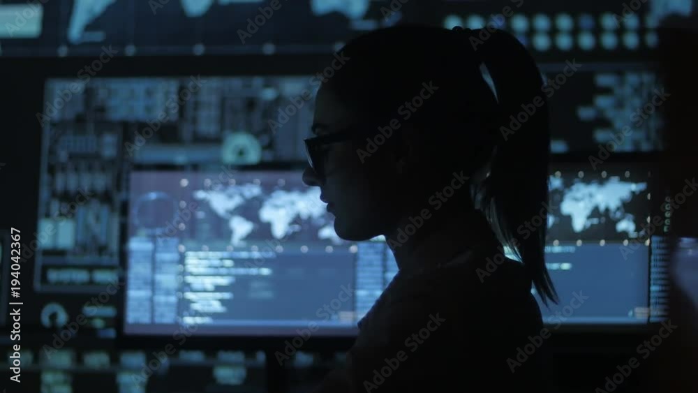 silhouette of young woman IT programmer working at a computer in the data center filled with display screens silhouette of young woman IT programmer working at a computer in the data center filled with display screens
