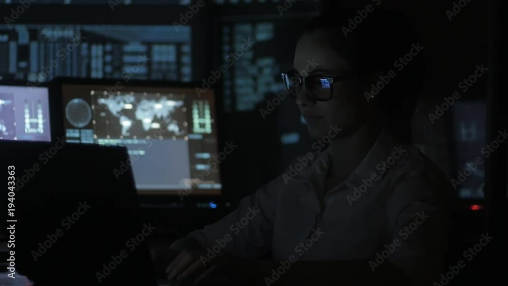 portrait of young woman programmer working at a computer in the data center filled with display screens portrait of young woman programmer working at a computer in the data center filled with display screens