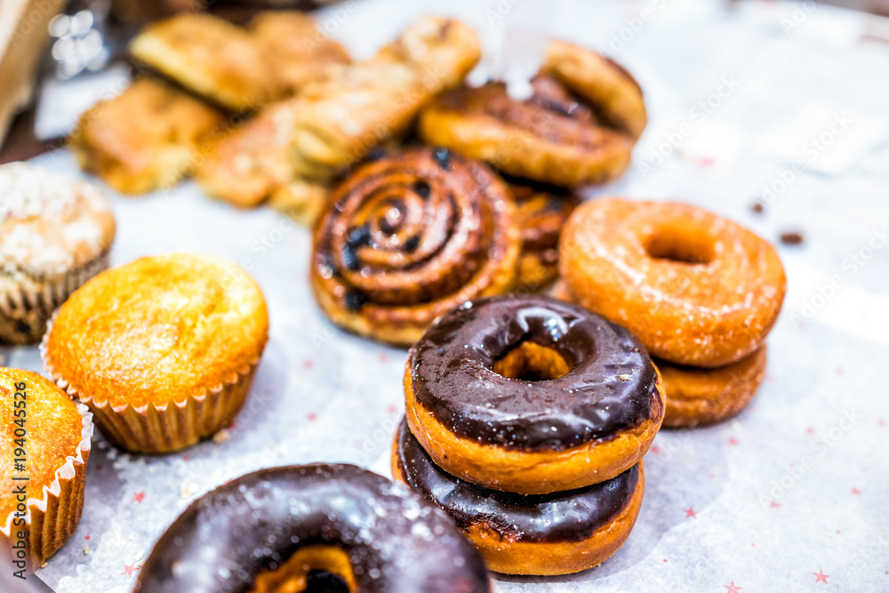 Many different selection of pastry dessert sweets for continental breakfast, chocolate fried donuts, muffins, cinnamon rolls buns on paper tray in cafe, store, brunch, buffet, home Many different selection of pastry dessert sweets for continental breakfast, chocolate fried donuts, muffins, cinnamon rolls buns on paper tray in cafe, store, brunch, buffet, home