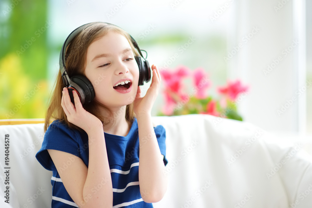 Cute little girl wearing huge wireless headphones. Pretty child listening to the music. Schoolgirl having fun listening to kid's songs at home. Cute little girl wearing huge wireless headphones. Pretty child listening to the music. Schoolgirl having fun listening to kid's songs at home.
