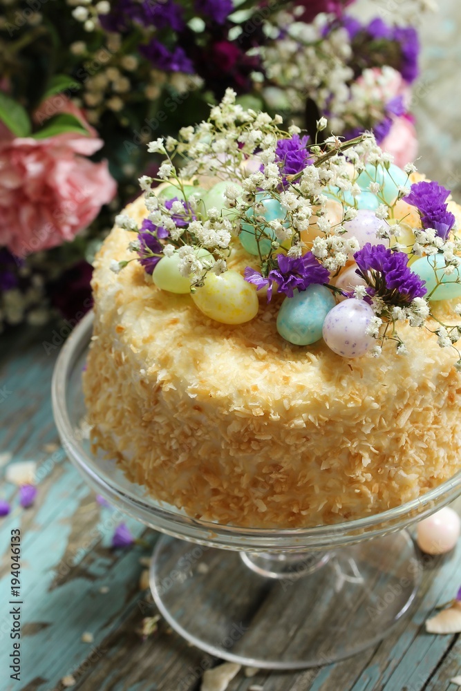 Homemade toasted coconut cake topped with easter egg candies and flowers, selective focus Homemade toasted coconut cake topped with easter egg candies and flowers, selective focus