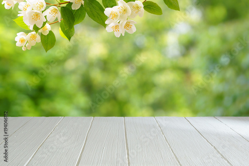 Empty white table with a blurred green background. White wooden table in the background of a summer garden. A branch of blossoming jasmine.