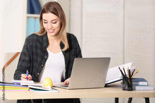 Pretty student with laptop studying at table indoors