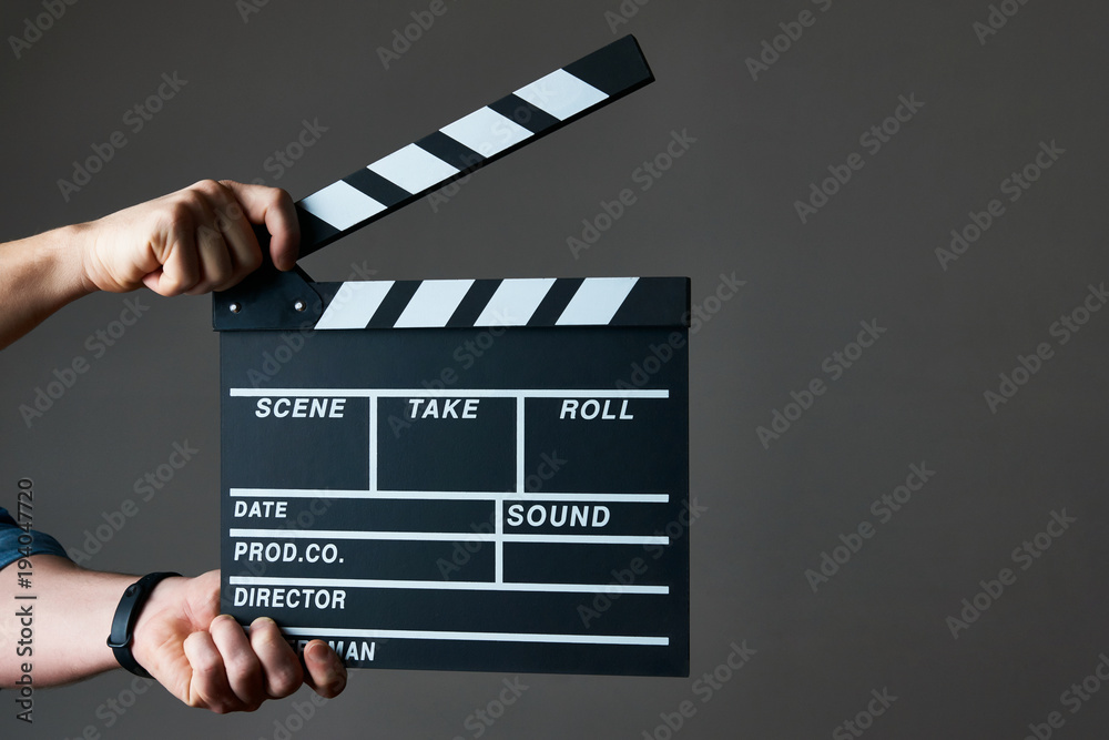 A movie production clapper board. Hands with a movie clapperboard on grey background with copy space, close-up. 