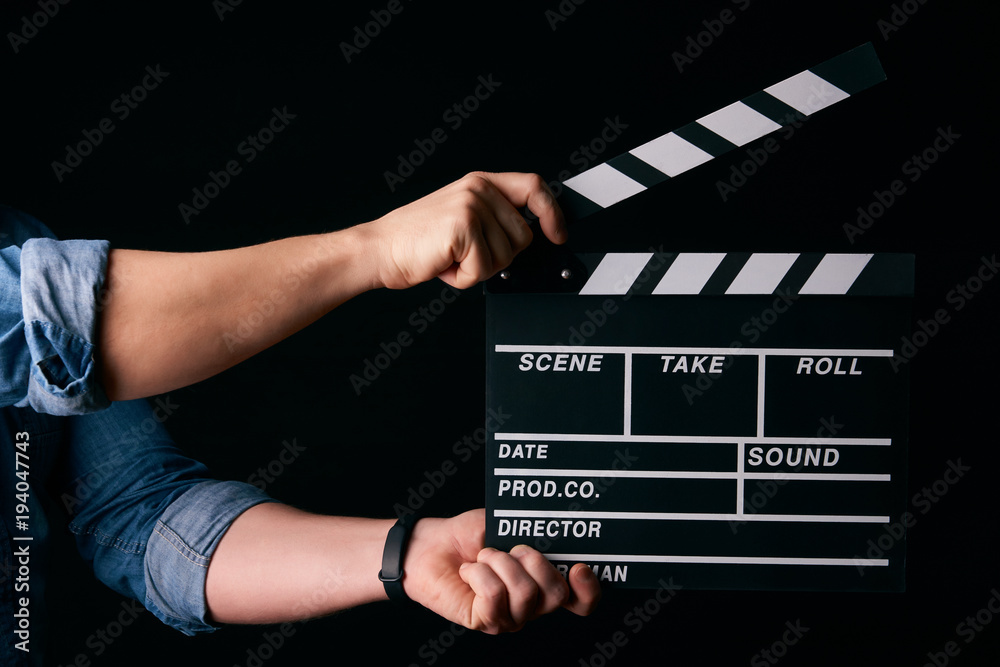 A movie production clapper board. Hands with a movie clapperboard on black background with copy space, close-up. 