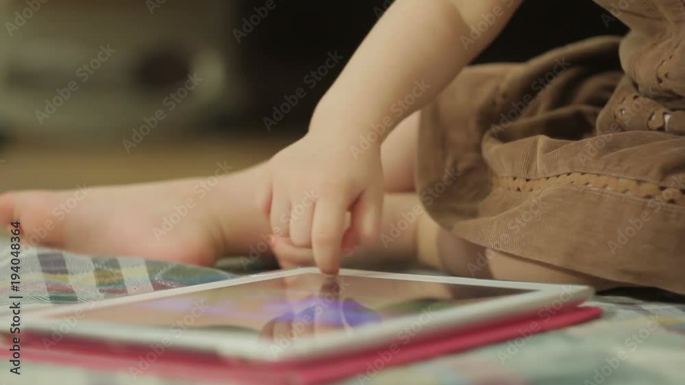 A little girl sitting on the floor uses a tablet PC, touching her finger on the touch screen A little girl sitting on the floor uses a tablet PC, touching her finger on the touch screen