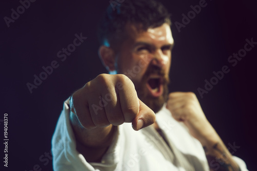 Strong arms and clenched fists. Portrait of screaming karate master instructor. Selective focus on fist. Brutal bearded man dressed in kimono practicing aikido. photo