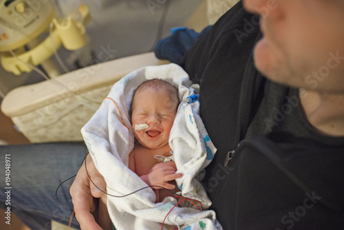 Father carrying newborn baby while sitting in hospital photo