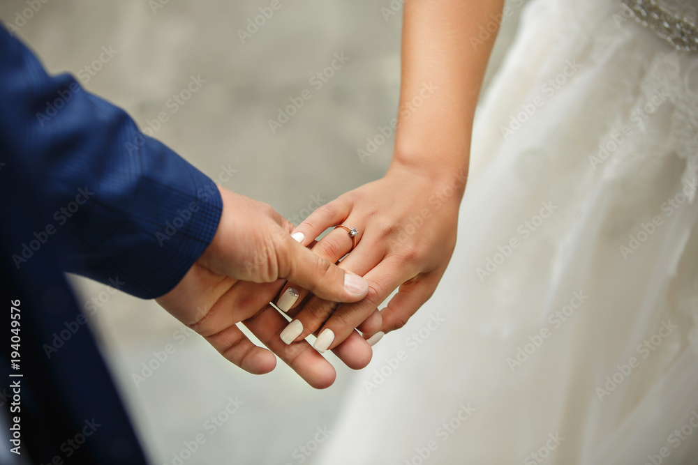 Bride and groom holding hands. Newlyweds couple in love at wedding day. Wedding and engagement ring on bride's hand. Happy marriage concept Bride and groom holding hands. Newlyweds couple in love at wedding day. Wedding and engagement ring on bride's hand. Happy marriage concept