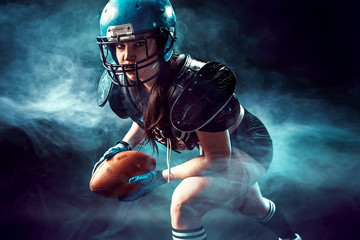 Sportive serious woman in helmet of rugby player holding ball in smoke.