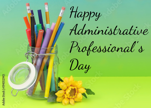 A clear hermetic jar filled with colorful makers and pencils on a graduated blue green blackground with yellow silk flower laying beside. Copy space.