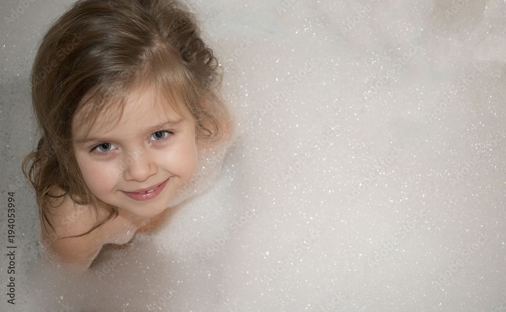 Happy smiling little girl sits in a bathroom with full foam Happy smiling little girl sits in a bathroom with full foam