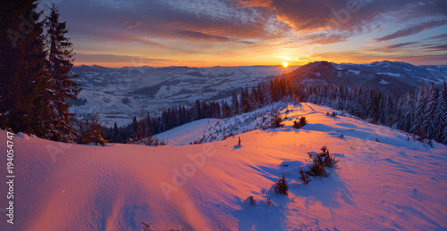 Wide panorama with beautiful sunrise in the winter Carpathians. Bright colorful sky. The mountains and the forest are covered with snow. © Володимир Гончарук