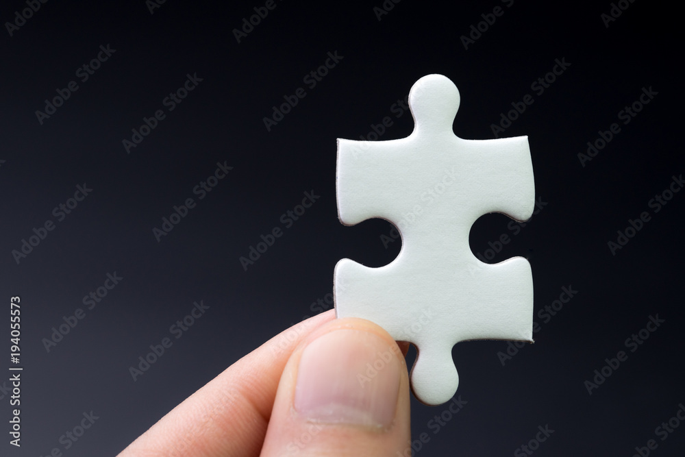 Obraz premium Business strategy missing piece, solution for success concept, hand holding a bright white paper jigsaw puzzle piece with dark black background
