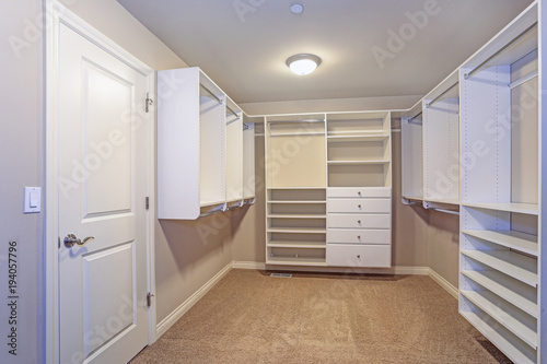 Large walk-in closet with white shelves, drawers photo