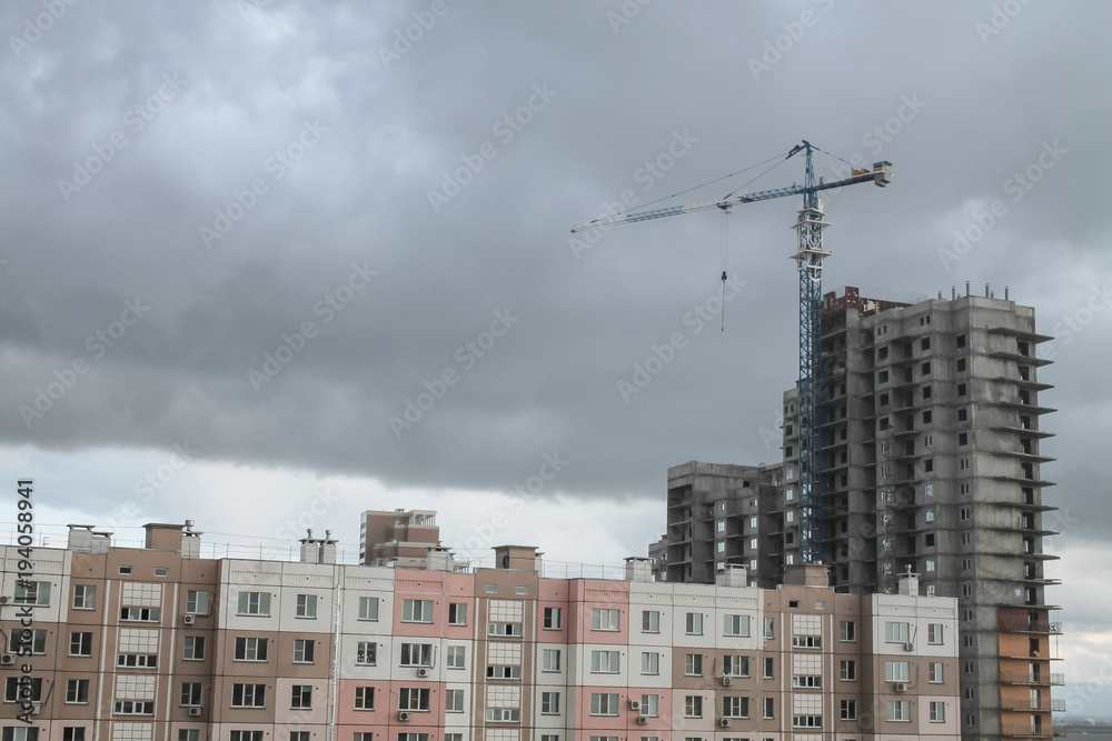 a crane standing over a tall block-of-flats with epic huge clouds on the background