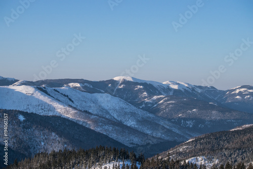 Winter landscape in the mountains with blue sky and snow-capped peaks and forest
