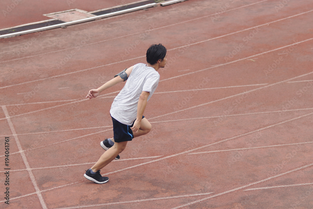 Young Asian sprinter leaving starting on racetrack at athletics stadium.